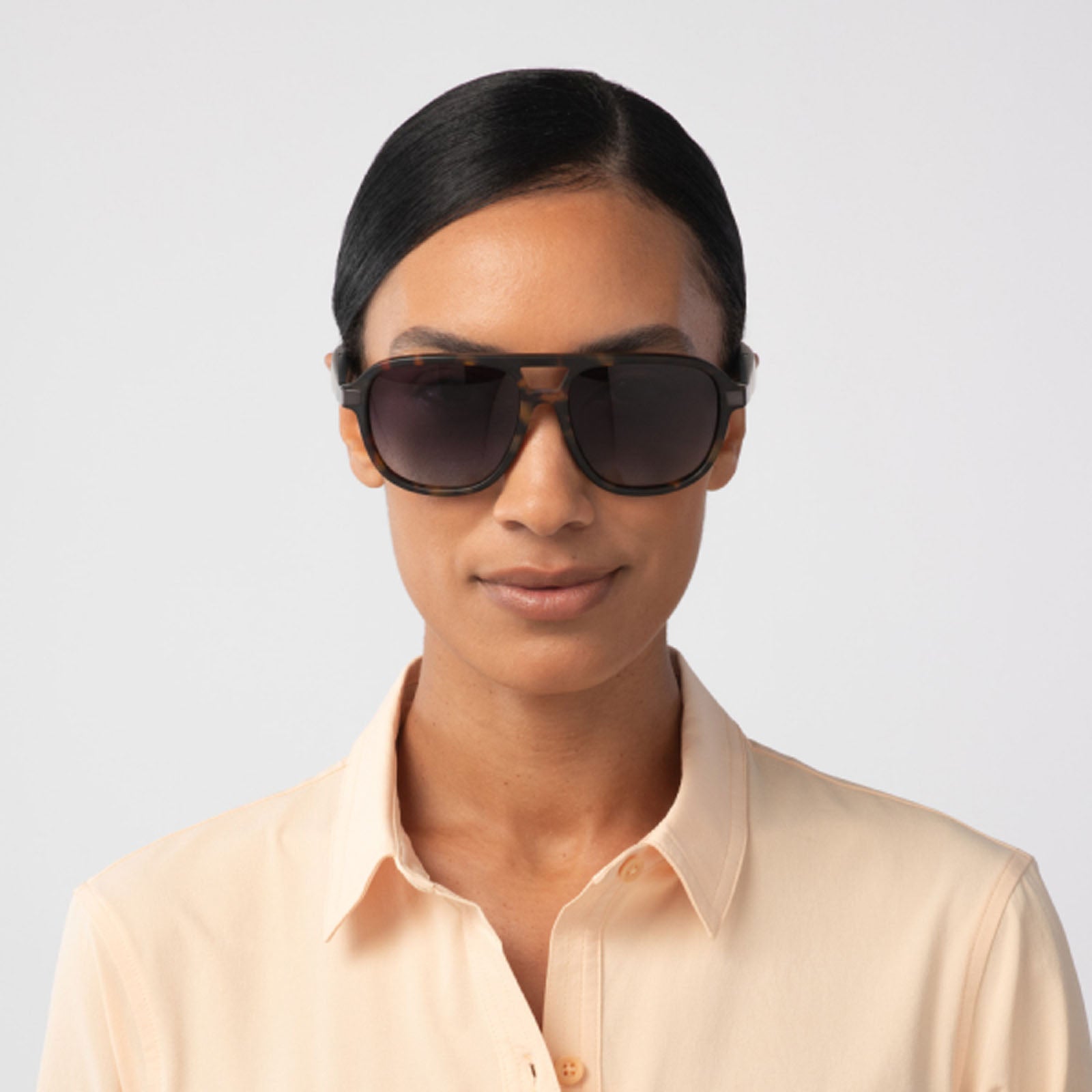 A person with smooth, dark hair pulled back wears Eddie Bauer Explorer polarized UV400 sunglasses and a light beige collared shirt, standing against a plain light background facing forward with a neutral expression.