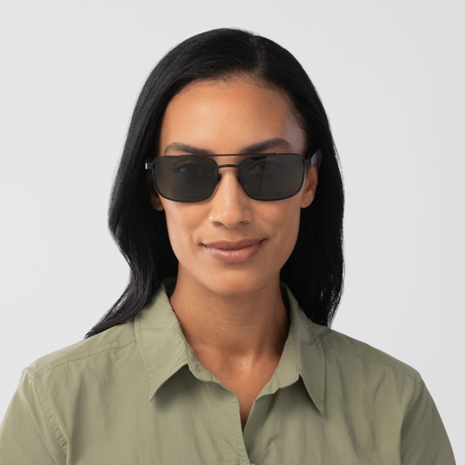 A woman with long black hair smiles softly, wearing Eddie Bauer Navigator UV400 polarized sunglasses and a light green collared shirt, set against a plain light background.