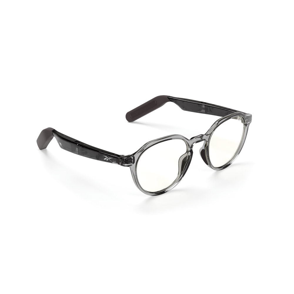The Reebok Jet eyewear features round, clear lenses and transparent gray frames with black temples that have textured grips at the ends. Shown on a white background, these glasses offer a stylish, privacy-focused design.