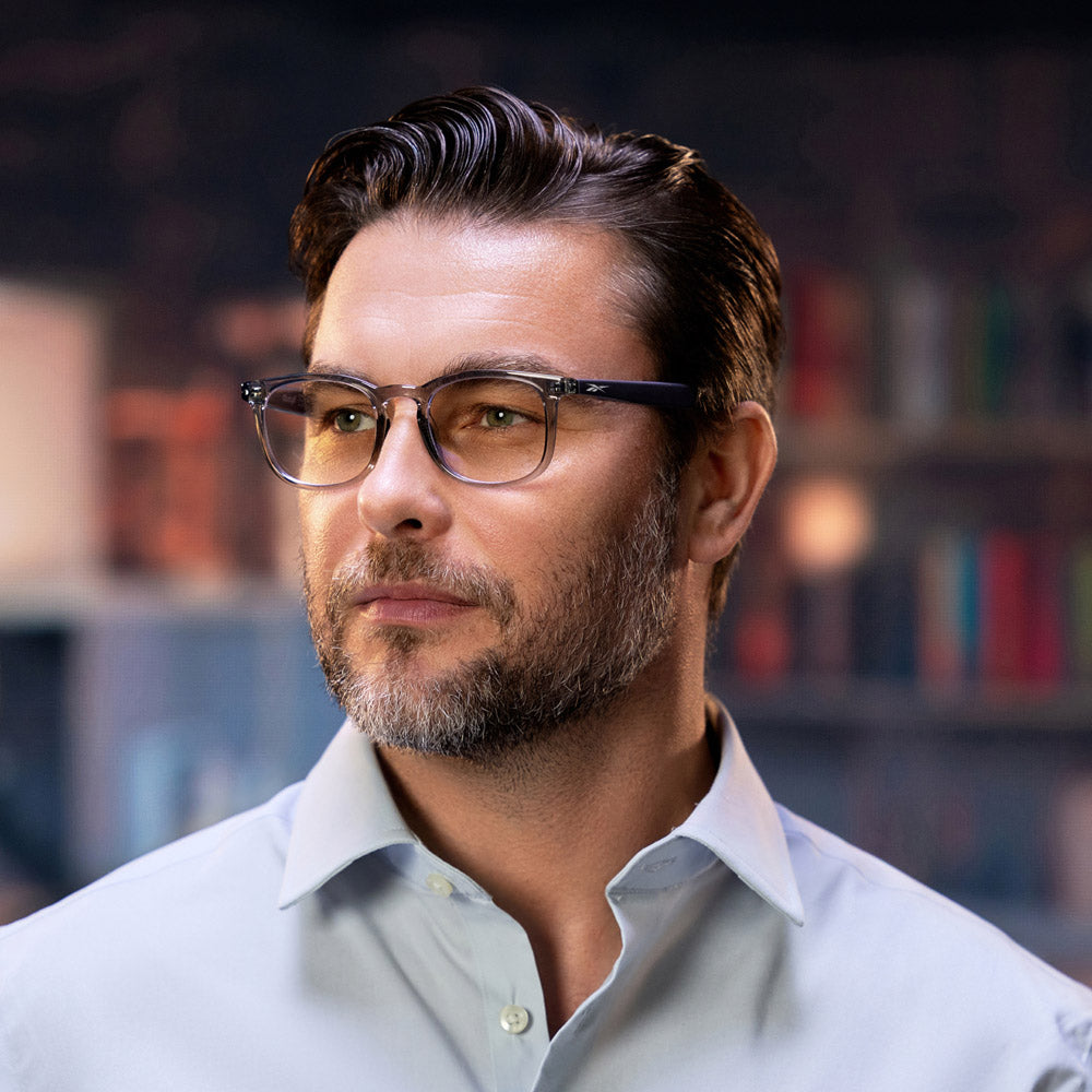 Reebok Thunder smart glasses, shown on a white background, feature clear, slightly tinted lenses, a transparent gray front frame, solid black arms, and open-ear audio technology.