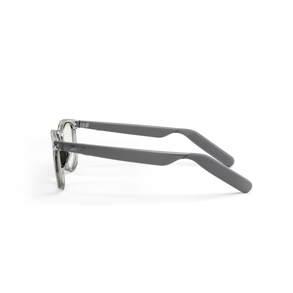 Side view of Reebok Thunder smart glasses with transparent round frames and solid gray temples on a white background—combining classic style and open-ear audio technology.