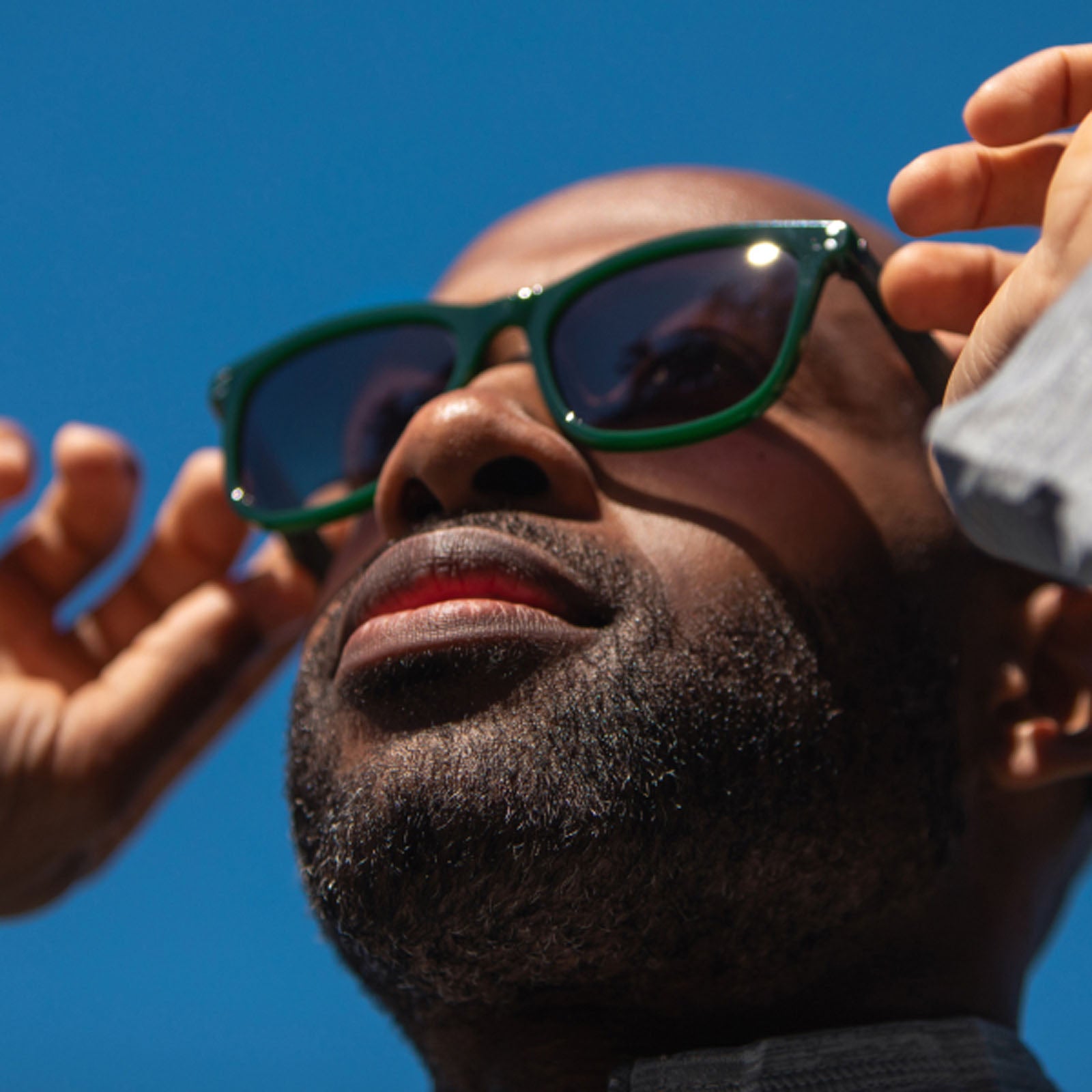 A close-up of a bearded man wearing Eddie Bauer Velocity UV400 polarized sunglasses, touching the frames with both hands against a clear blue sky.